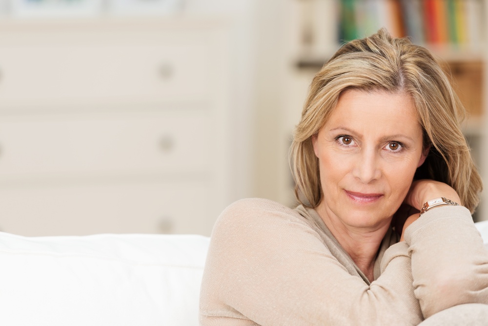 Attractive sincere middle-aged woman sitting on a sofa leaning her head on her raised arm looking directly at the camera with a serious expression